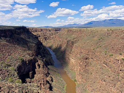 The 600 plus foot gorge of the Rio Grande river cutting through New Mexico near US 64. Scattered cumulus clouds paint shadows over the gorge.
