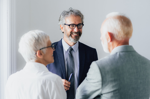 Shot of three senior coworkers having a discussion in office. Mature Corporate business persons having discussion and sharing ideas standing  in the workplace.