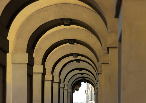Corridor with rows of columns and arc in sunlight, Detail of the corridor along the Arno river, near the Ponte Vecchio, Florence