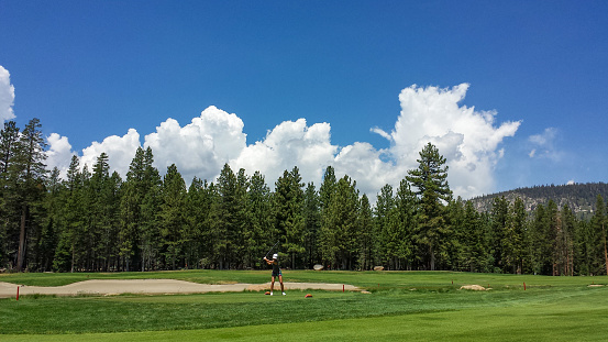 A wide shot of a woman golfer in the distance on a beautiful day in California.