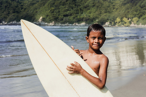 latin child boy with surfboard on the beach in Mexico Latin America, hispanic people surfing in summer sport activity