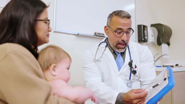 Doctor speaks with a young woman holding her baby girl at the appointment reviewing the growth chart