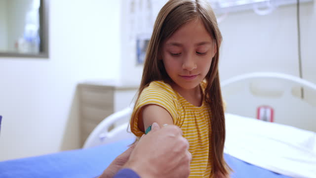Nurse applies a bandaid to a girl who just received a vaccine
