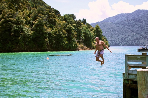 A man jumps from jetty into the sea in summer. Taken in the Marlborough Sounds of New Zealand's South Island.