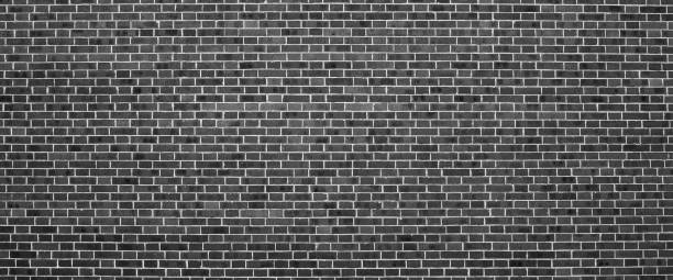 istock Grayscale backdrop with old realistic black brick wall. Minimal fragment of brickwall close-up. Minimalist monochrome background with wall of gray bricks in different shades. Simple wall texture. 1504759476