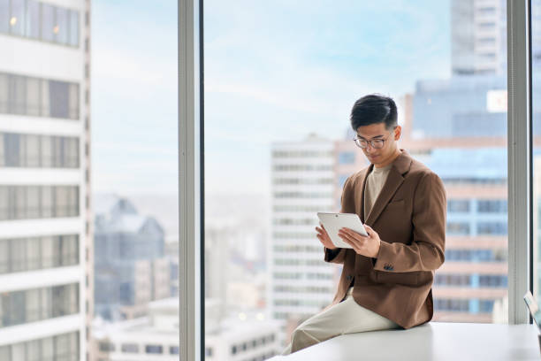 istock Young Asian business man executive using tablet sitting in modern office. 1504764057