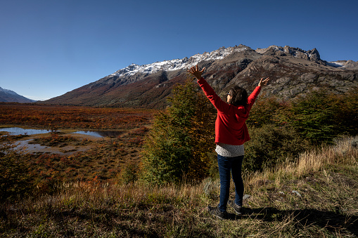 Woman from behind with her arms raised in front of an imposing landscape in the area of El Chalten, Santa Cruz, Argentina.