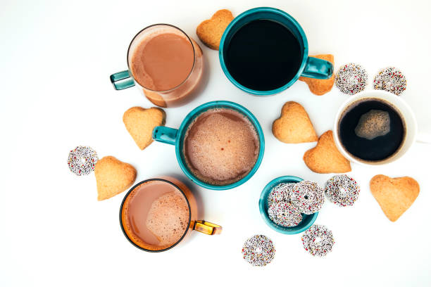 Mugs of coffee with foam and a plate with heart-shaped shortbread cookies on a white background stock photo