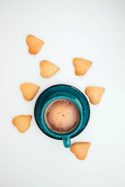 A cup of coffee with foam and a plate with heart-shaped shortbread cookies on a white background stock photo