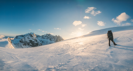 Panorama of mountaineer climbing to the top of snowy mountain and sunset shining in winter at Mount Ryten, Lofoten Islands, Norway