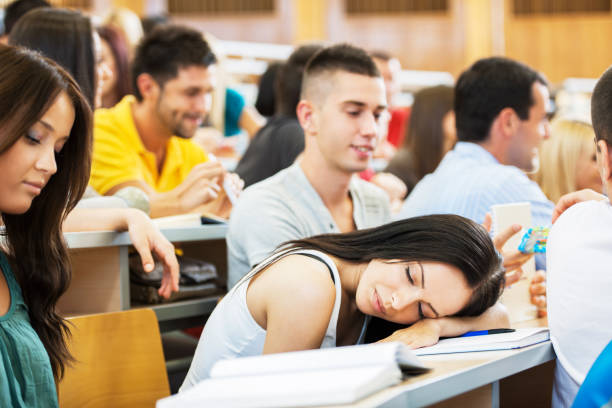 Young female student sleeping during a lecture. Large group of college students sitting in the university amphitheatre. The focus is on the woman sleeping. male college student sleeping through lecture stock pictures, royalty-free photos & images