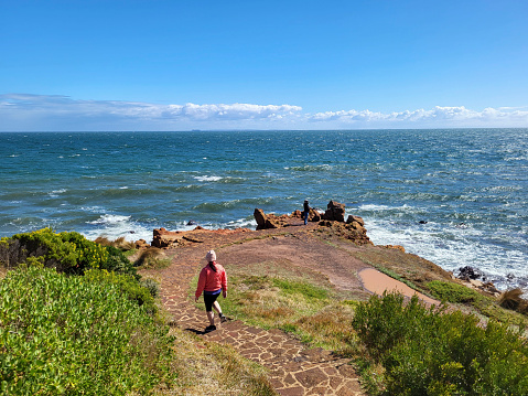 Mornington, Australia: April 08, 2023: Tourists looking at the waves from the path at Mornington Peninsular overlooking Port Phillip Bay. The boardwalk path is very popular because of the beautiful views of the ocean and interesting geology along the bay.
