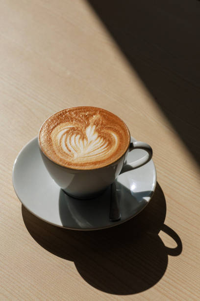 filiżanka kawy latte na drewnianym stole tworzy cień w silnym świetle słonecznym. - craft zdjęcia i obrazy z banku zdjęć