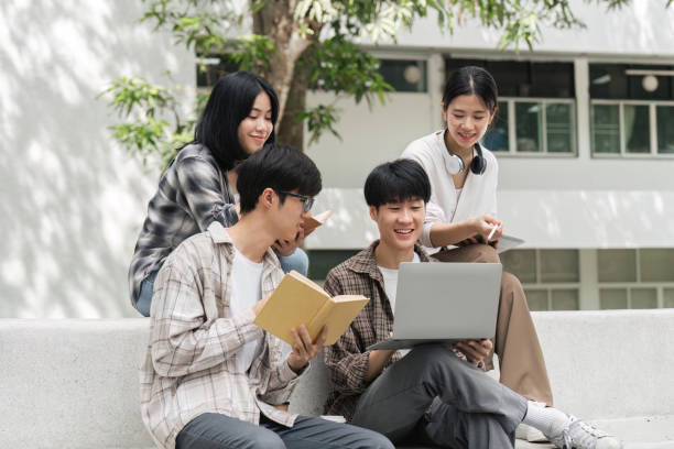 Group of happy students checking results on laptop and tablet while sitting on college campus, concept of education, technology and project work discussion