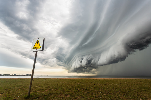 Massive shelf storm cloud with rain below over the ocean with a danger sign