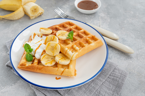 Waffles with banana, whipped cream and salty caramel on a gray concrete background