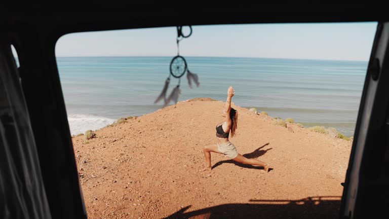 ZI/O Woman doing yoga in front of her camper van parked on the beach by the sea