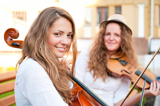 Two women strings duet playing violin and cello on the street of european city