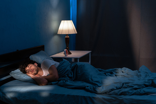Young arabic man sleeping in bed at home at night. People, bedtime and rest concept. Copy space