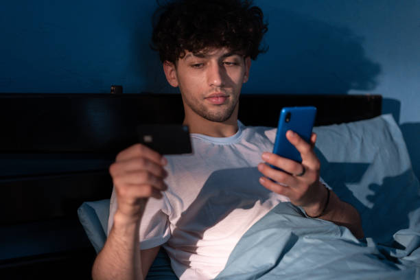 istock Young man holding credit card and using cellphone for Online shopping, e-shopping. Arab guy lying in his comfortable bed at night and buying online in internet 1505093665