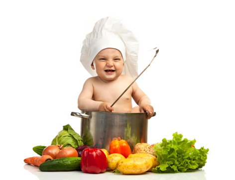 Little boy in chef's hat with ladle, casserole, and vegetables, over white background