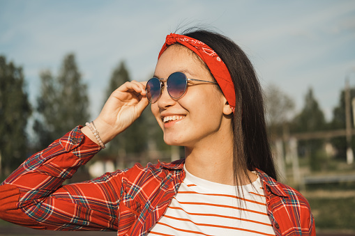 Close-up image of nice-looking young asian girl in sunglasses outdoors. Cheerful brunette student girl smiles and enjoying a sunny summer day. Summer vacation concept