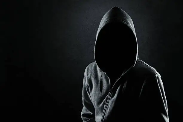 Silhouette of hooded man or hooligan over dark concrete background with copy space