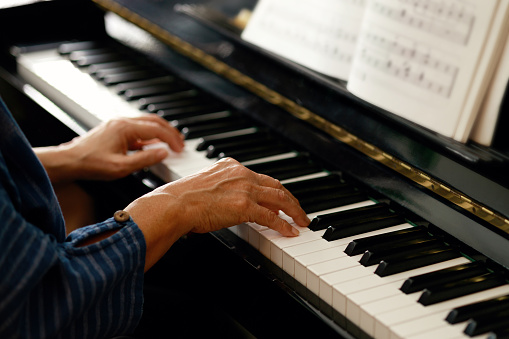 Close-up of a senior Asian woman playing the piano in her home, spending quality time learning the instrument after retirement.