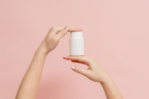 istock Plastic bottle (tube) in hands on pink background. Packaging for vitamins, tablets or capsule, or supplement 1505225912