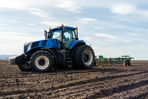 A tractor with seedbed cultivator ploughs field on morning.