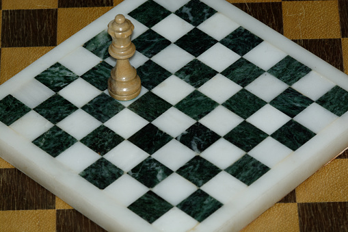 A beautiful handmade, hand-stained wooden checkerboard and checkers sits ready for a game. Nice woodgrain detail throughout. Sitting on an arborite countertop which has a slightly textured, rich green matte finish and is NOT completely smooth. Strong lighting highlights the board, and softens the surrounding area.