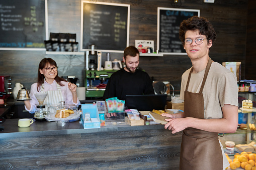 Coffee shop workers, a young guy in an apron in focus. Small business cafe cafeteria coffee house, job, work, staff people concept
