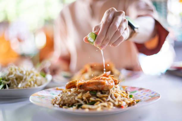 Hand with lime sliced squeezed to pad thai shrimp for add a sour taste to cooking delicious Thai food.