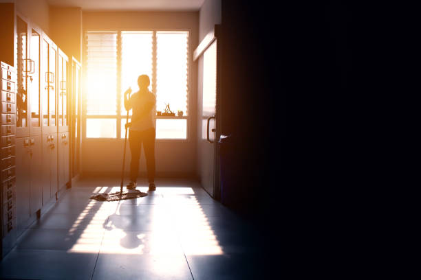 Janitor woman mopping floor in hallway office building or walkway after school and classroom silhouette work job with sun light background. Poor people working job.