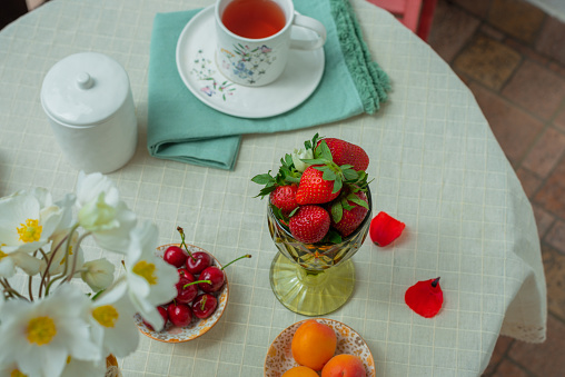 Fruit tea, berries and wild flowers bouquet on white tablecloth