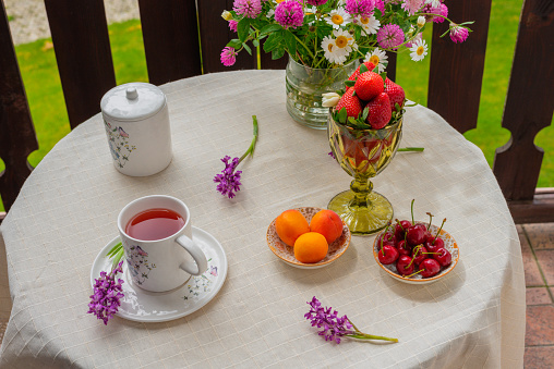 Fruit tea, berries and wild flowers bouquet on white tablecloth