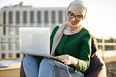 Lady in hijab putting charge cable into laptop outdoors