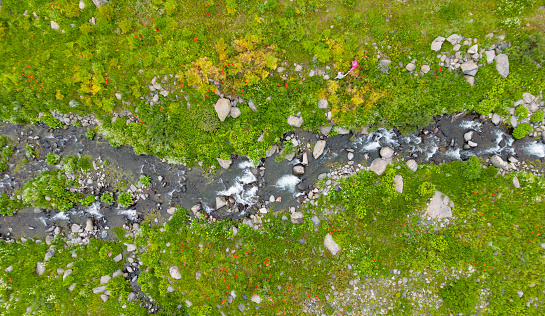 Aerial view mountain stream with colourful stones. Flowing river with smooth stones. Spring water running through different stones.