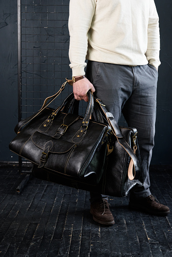 a man with bags. two different size black leather travel bags, indoors photo on black background.