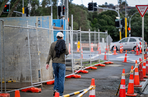 Man walking on sidewalk with orange traffic cones on one side and concrete blocks on the other side. Roadworks in Auckland.