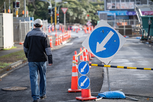 Man walking on the road with orange traffic cones diverting the traffic. Road under maintenance. Auckland.