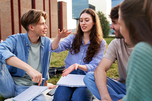 Group of caucasian students sitting outside the university campus and studying together