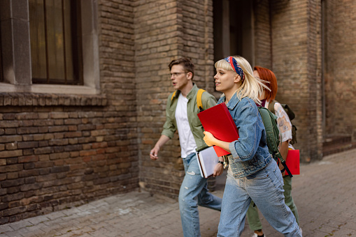 Group of university students running on the street while being late for class. Focus is on blond woman.