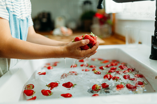 Boy holding strawberries in his hands and washing them with running water in the kitchen sink