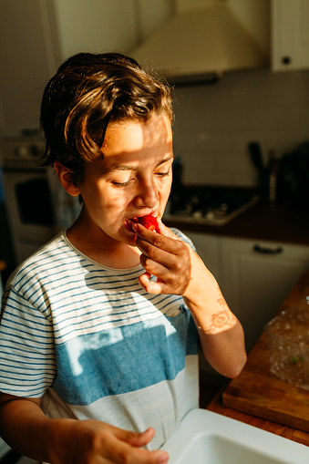 Boy tasting fresh washed strawberries that he washed in the kitchen sink