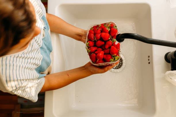 junge hält schüssel voll mit erdbeeren und wäscht sie in der küchenspüle - washing fruit preparing food strawberry stock-fotos und bilder