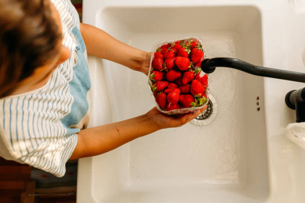 딸기로 가득 찬 그릇을 들고 부엌 싱크대에서 씻는 소년 - washing fruit preparing food strawberry 뉴스 사진 이미지