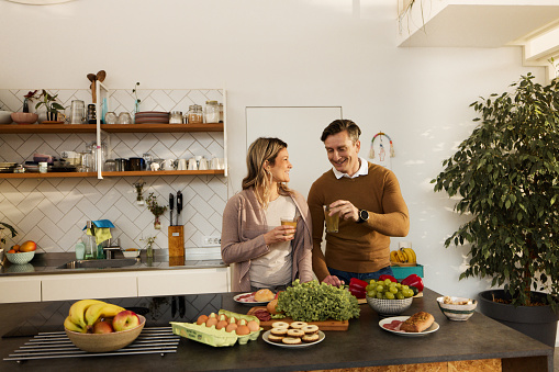 Happy mid adult couple enjoying in juice while having breakfast in the kitchen.