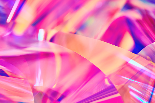 Close-up of ethereal bright neon pink, magenta, orange, blue, purple holographic metallic foil background. Abstract modern curved blurred surreal futuristic disco, rave, techno, festive backdrop