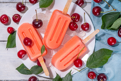 Cherry yoghurt ice cream lollypops, Homemade berry fruit popsicles with fresh cherries, white wooden background copy space
